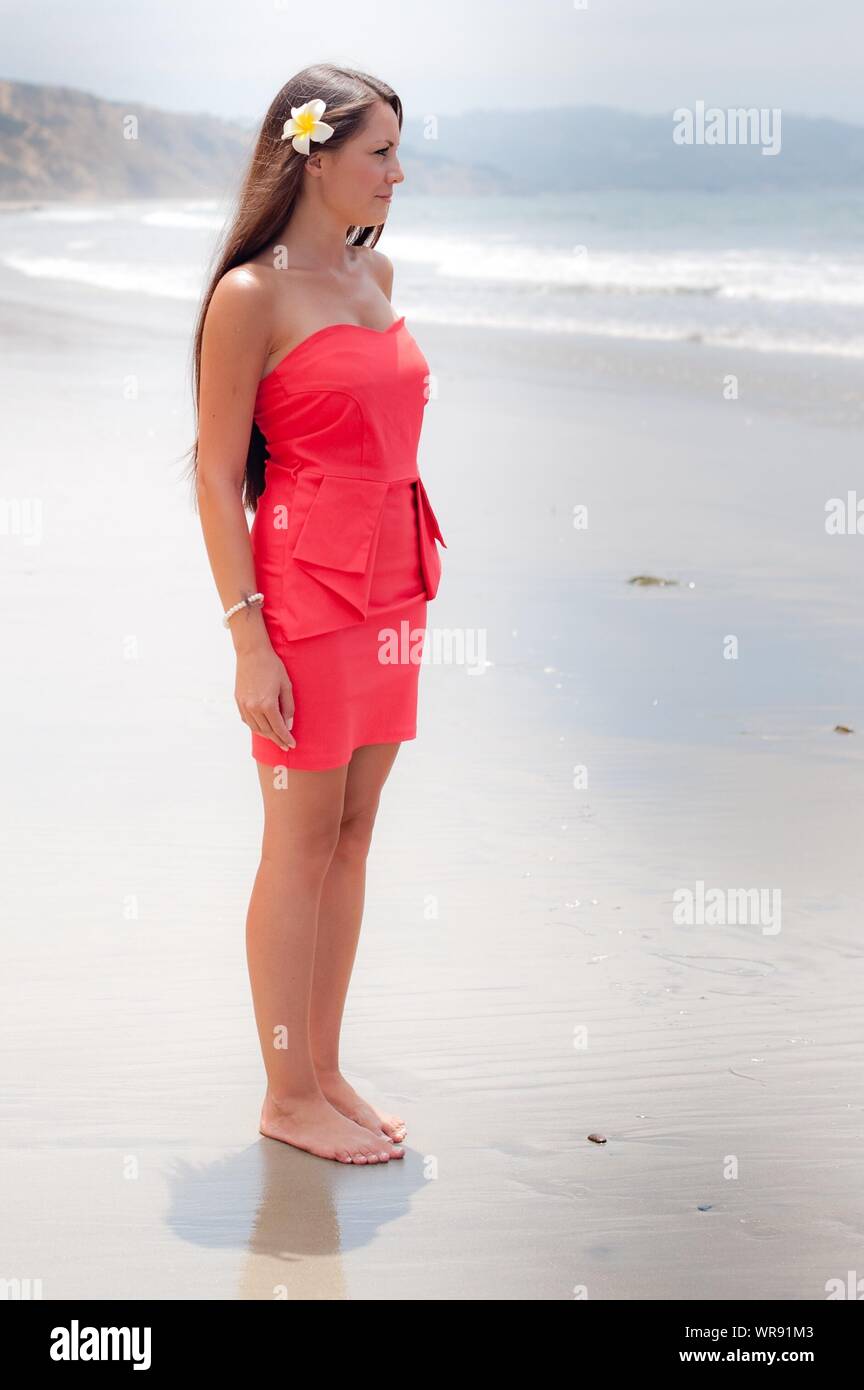 Hermosa Joven en Mini Vestido Rojo de pie en la playa contra el cielo  Fotografía de stock - Alamy