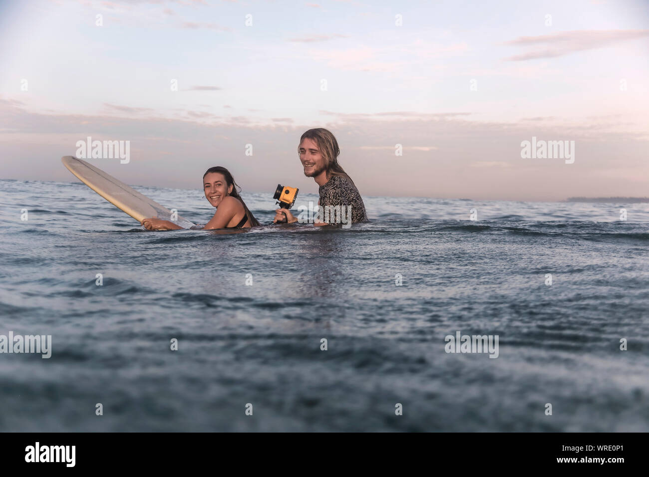 Feliz pareja con tabla de surf y cámara en Ocean Foto de stock
