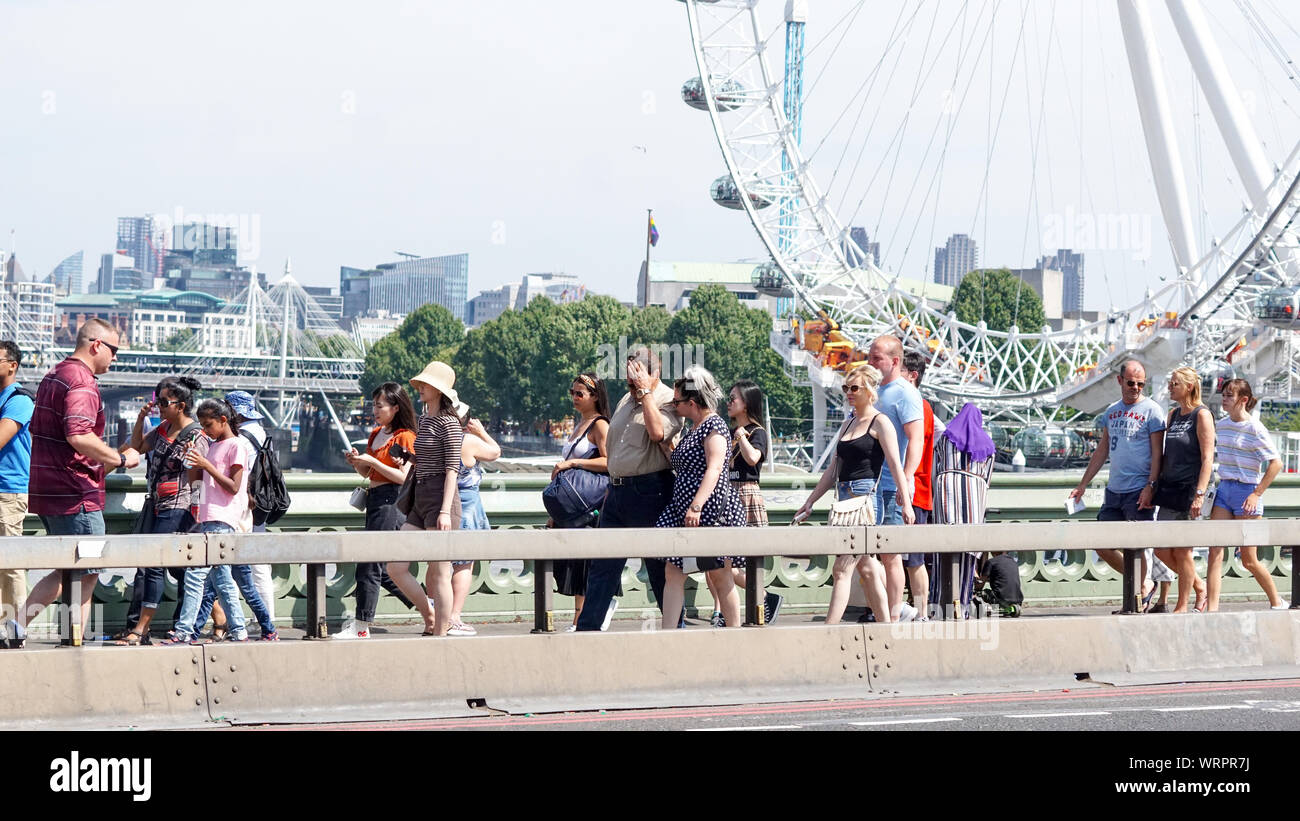 Los peatones caminar en Westminster Bridge, como se ve en el fondo de ojo de Londres en un día caluroso en el centro de Londres. Foto por Foto de stock