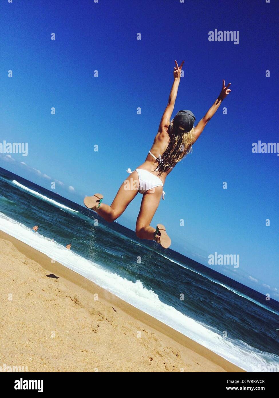 Vista trasera de la joven mujer vistiendo Bikini saltando en la playa Foto de stock