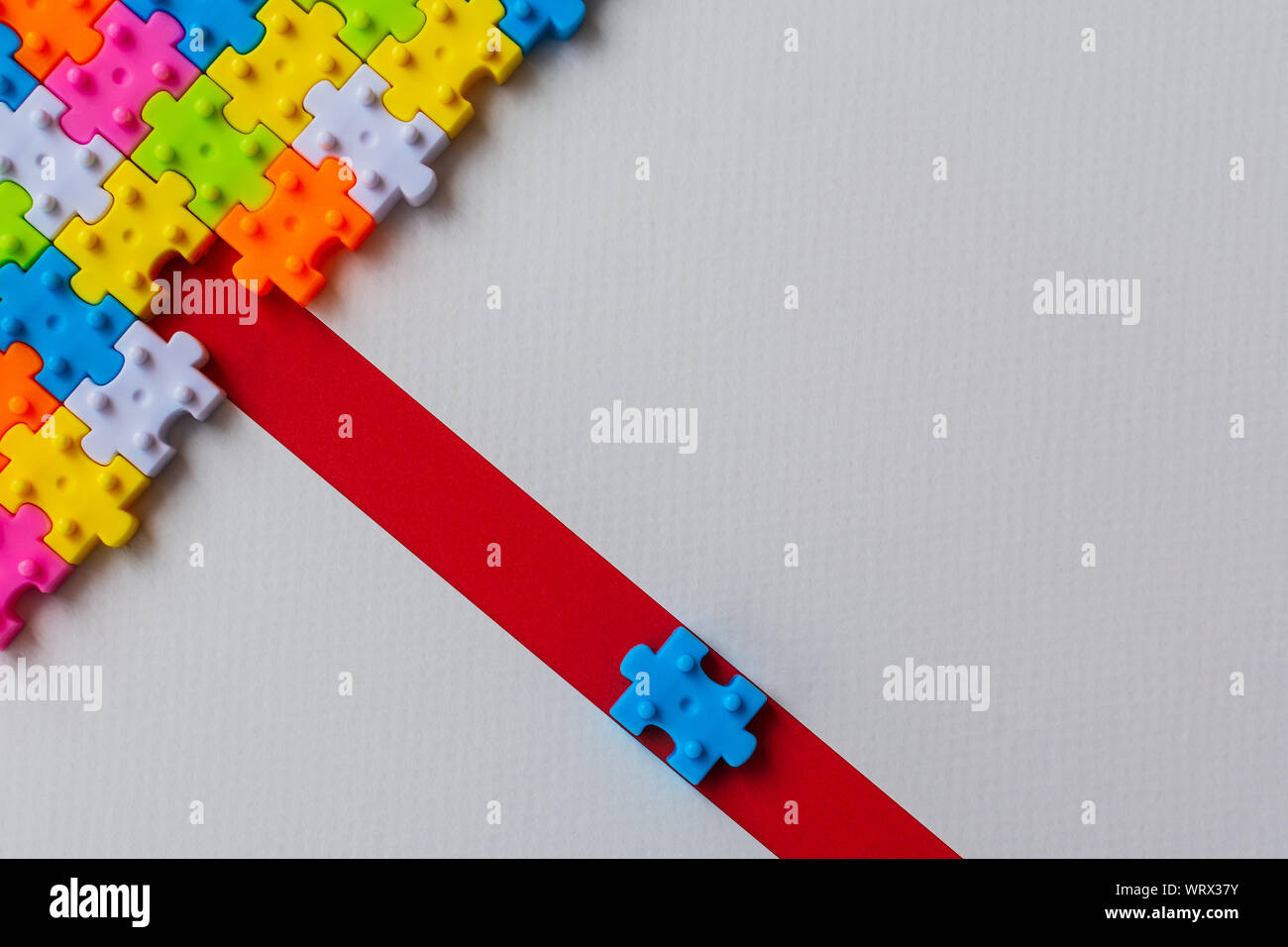 Puzzle de plástico de colores sobre papel blanco de fondo, falta un rompecabezas en línea roja para completar con copia espacio, estrategia empresarial trabajo en equipo Foto de stock