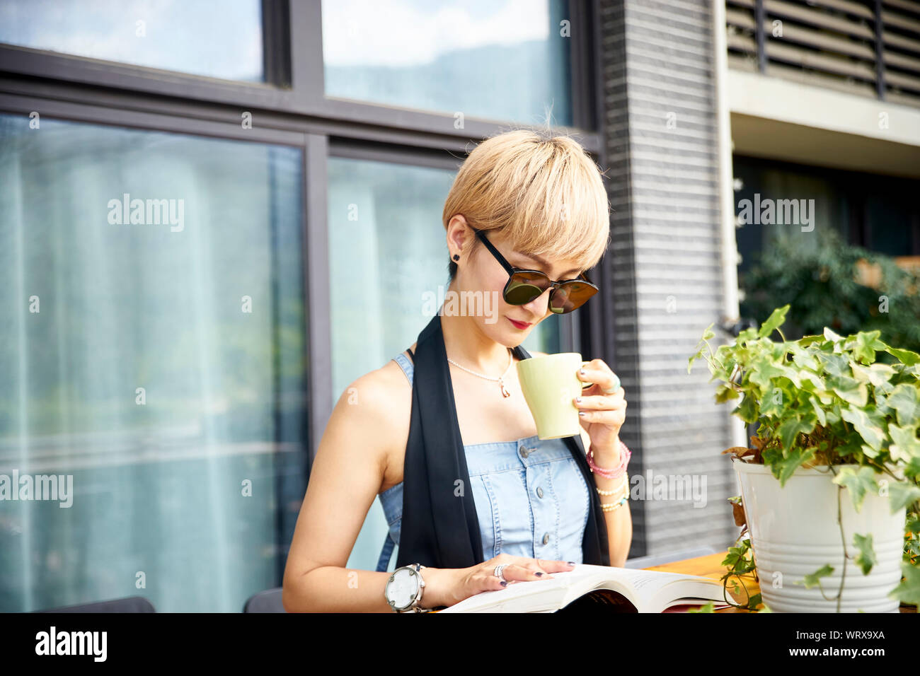 Joven mujer asiática disfrutando de la lectura y el café en el patio Foto de stock