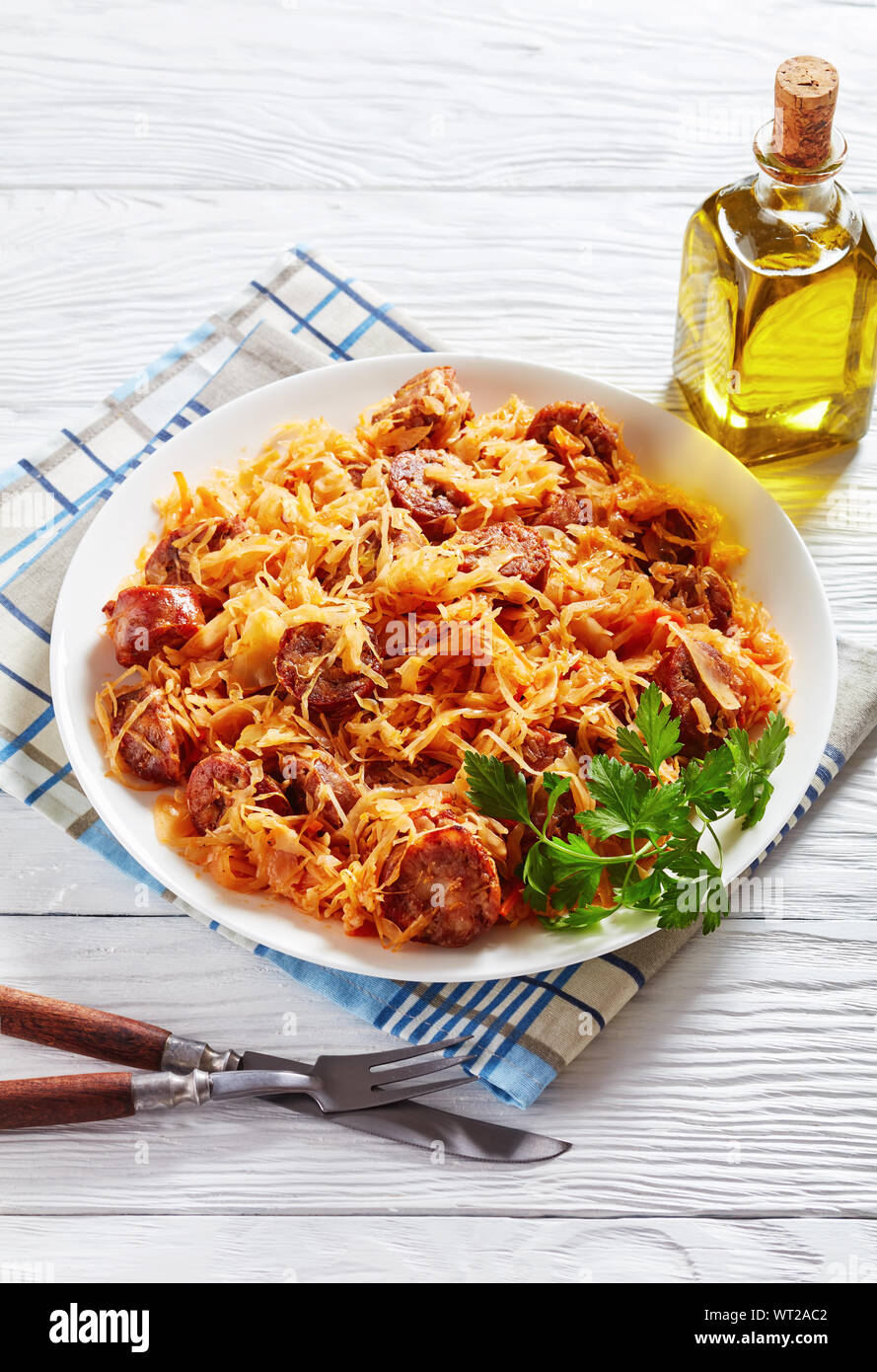 El estofado de col con rodajas de salchichas asadas servidos en un plato blanco en una mesa de madera, vista vertical desde arriba Foto de stock
