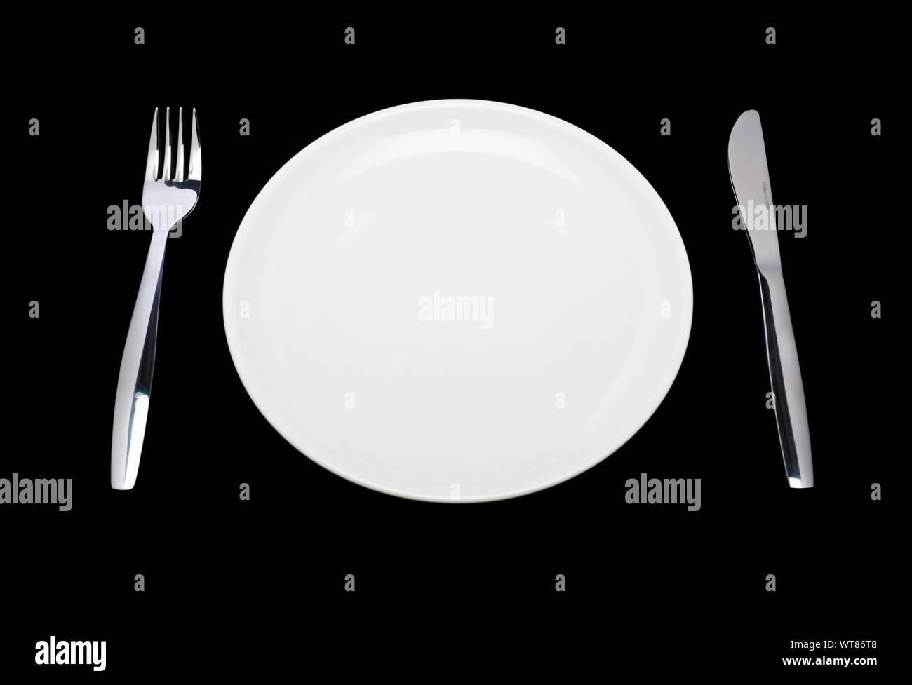 Place Setting, placa blanca, cuchillo y tenedor sobre un fondo negro Foto de stock