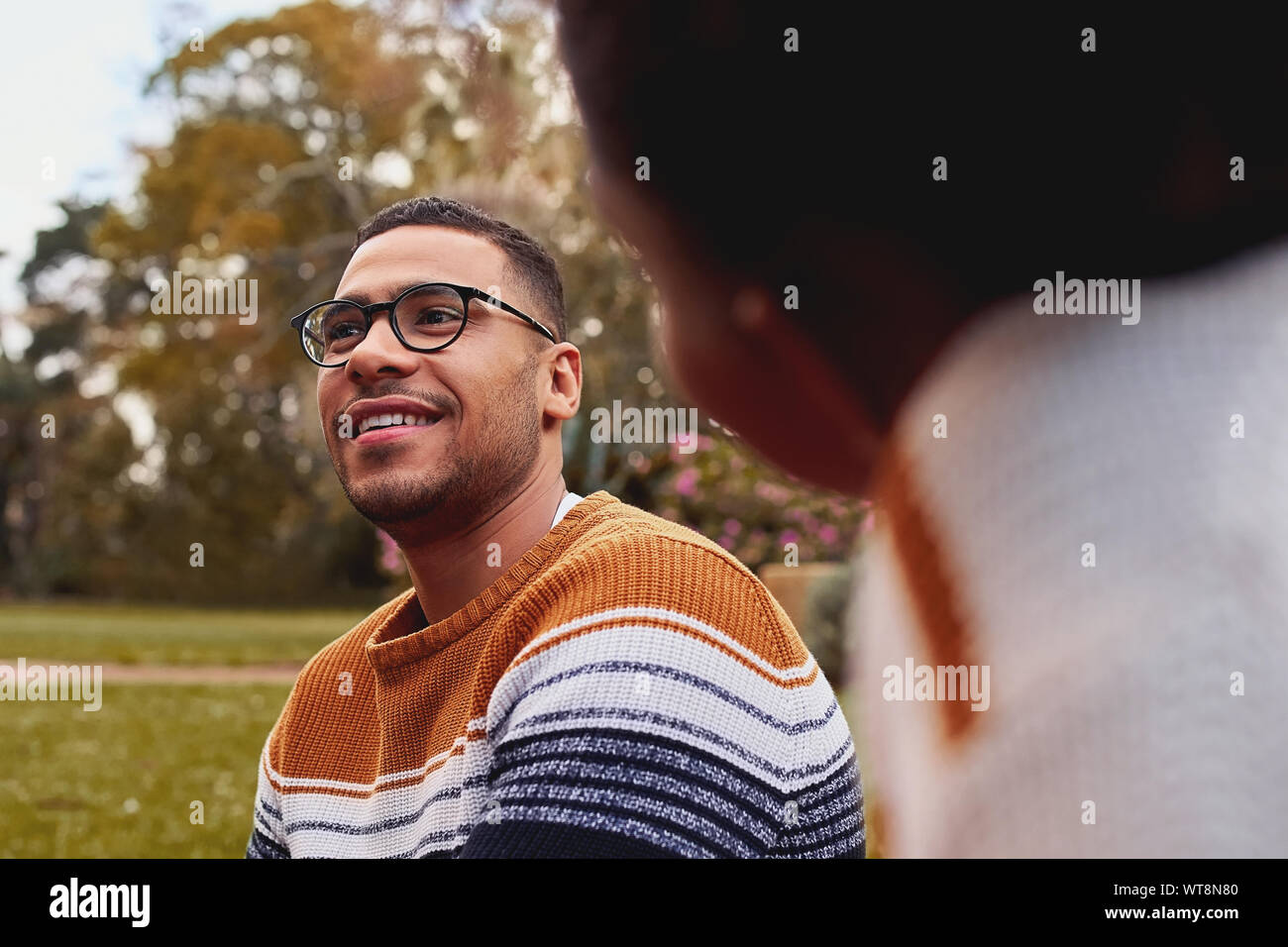 Cerca de una sonriente joven hombre africano el uso de anteojos, sentado con su novia en park Foto de stock
