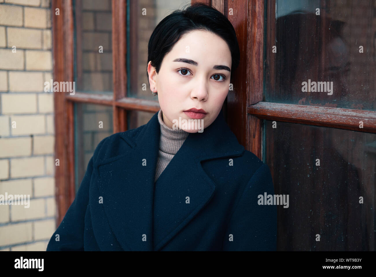 Close Up Retrato De Una Mujer Morena De Moda Con El Pelo Corto Y Vistiendo Una Capa Azul Sobre El Fondo De Un Marco De Puerta Adorable Chica Milenario Fotografia De Stock