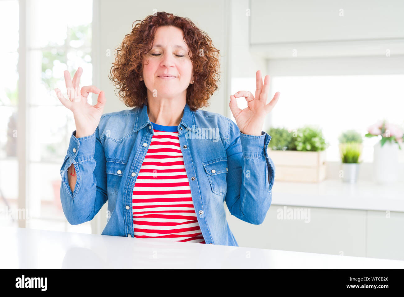 Edad media mujer mayor con el pelo rizado vistiendo de dril de algodón en relajado sonriendo con los ojos cerrados, hacer meditación gesto los dedos. Yoga Fotografía de