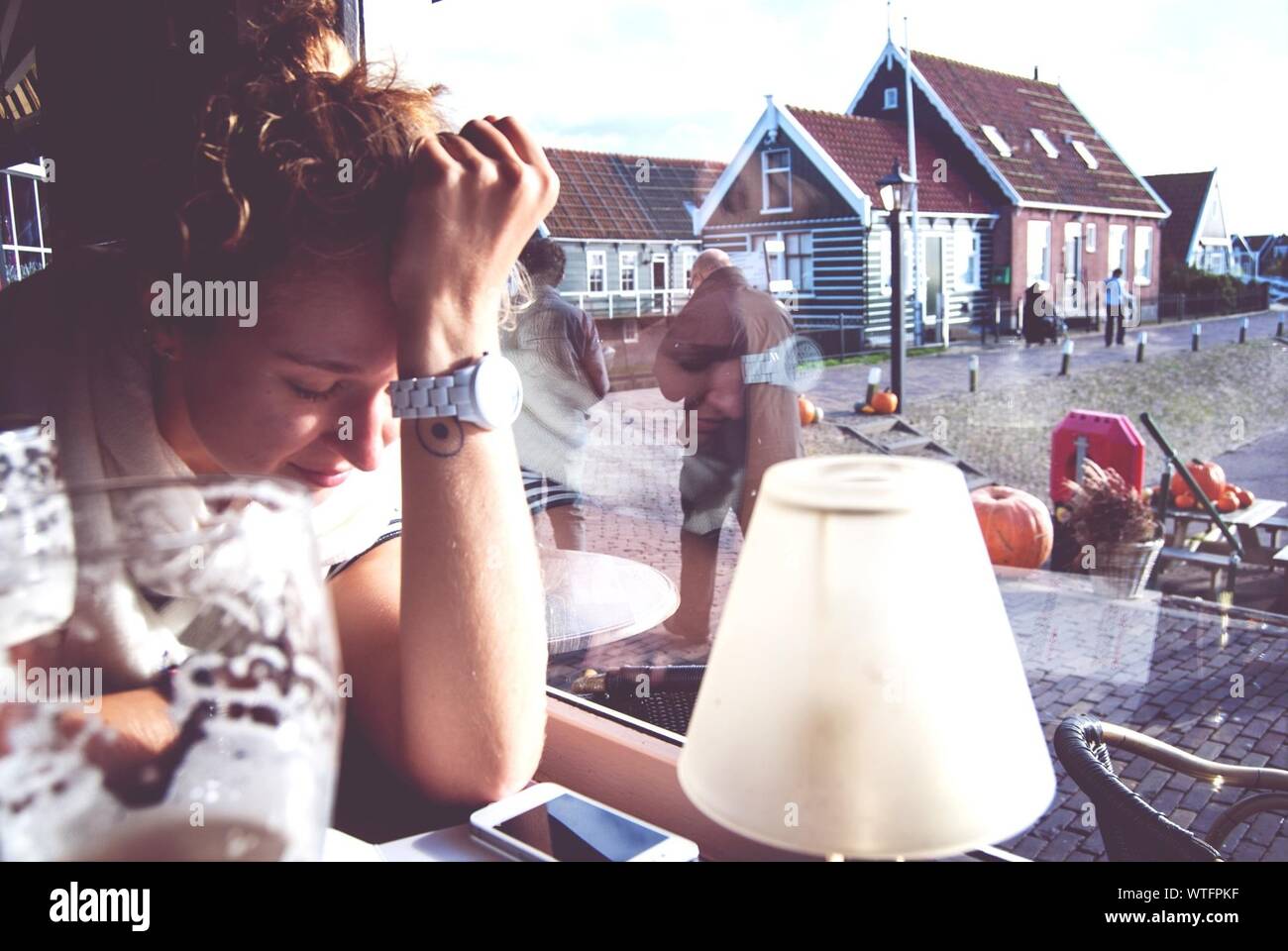 Estresante Mujer sentada en el Café contra casas visto a través del cristal de la ventana Foto de stock