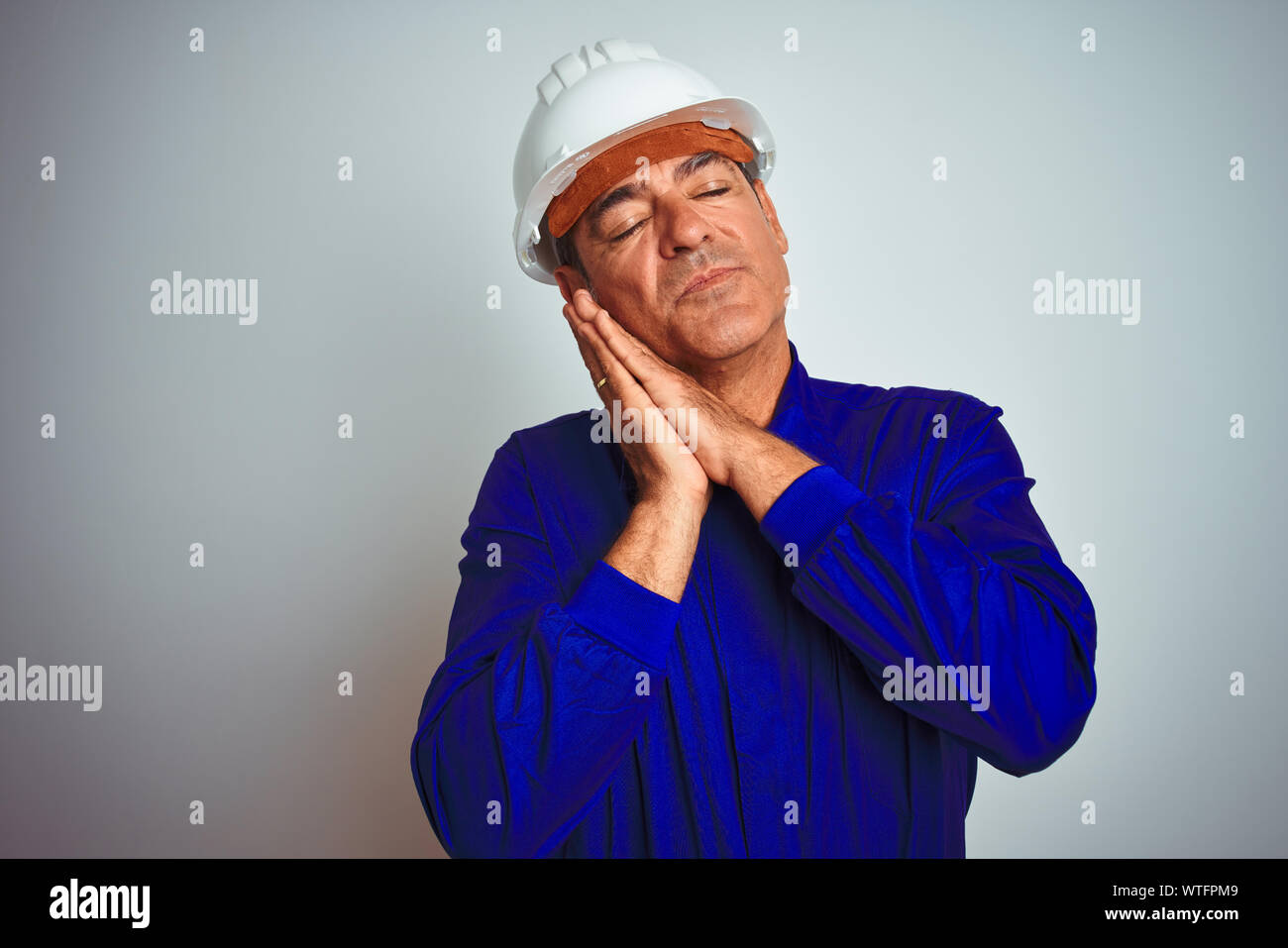 Apuesto trabajador de mediana edad hombre con uniforme y casco aislados sobre fondo blanco durmiendo Cansado de soñar y posando con las manos juntas mientras Fotografía de stock - Alamy