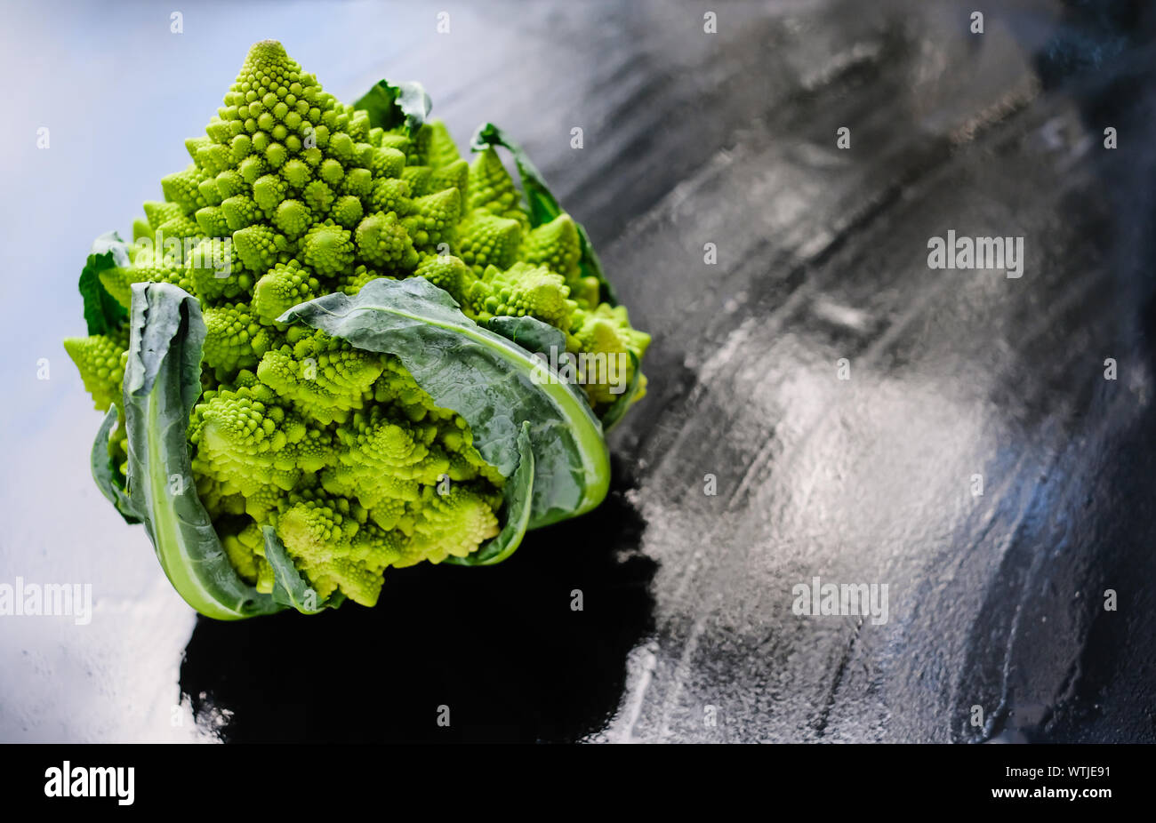 Increíble brócoli romanesco verde fresco o coliflor romana sobre fondo húmedo oscuro. Su forma es una aproximación natural de un fractal. Vista de primer plano. Foto de stock