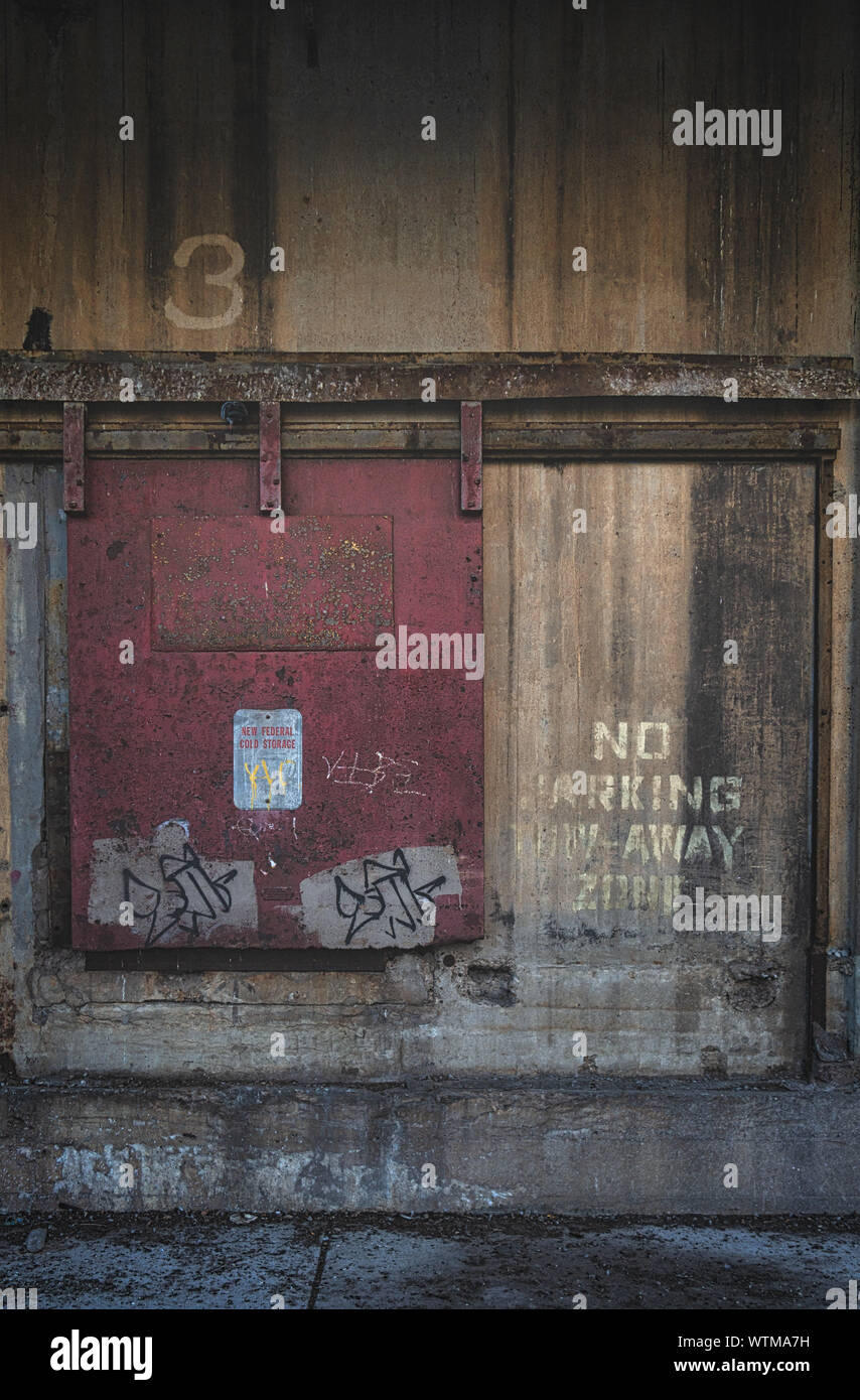 Una puerta roja cerrada en el exterior de un antiguo edificio industrial que dice 'Zona de salida de aparcamiento' Foto de stock