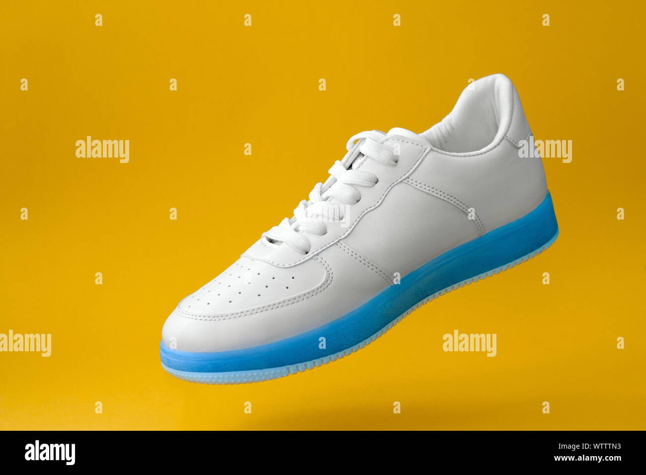 Moda sneakers blanco con azul único aislado sobre fondo amarillo Foto de stock