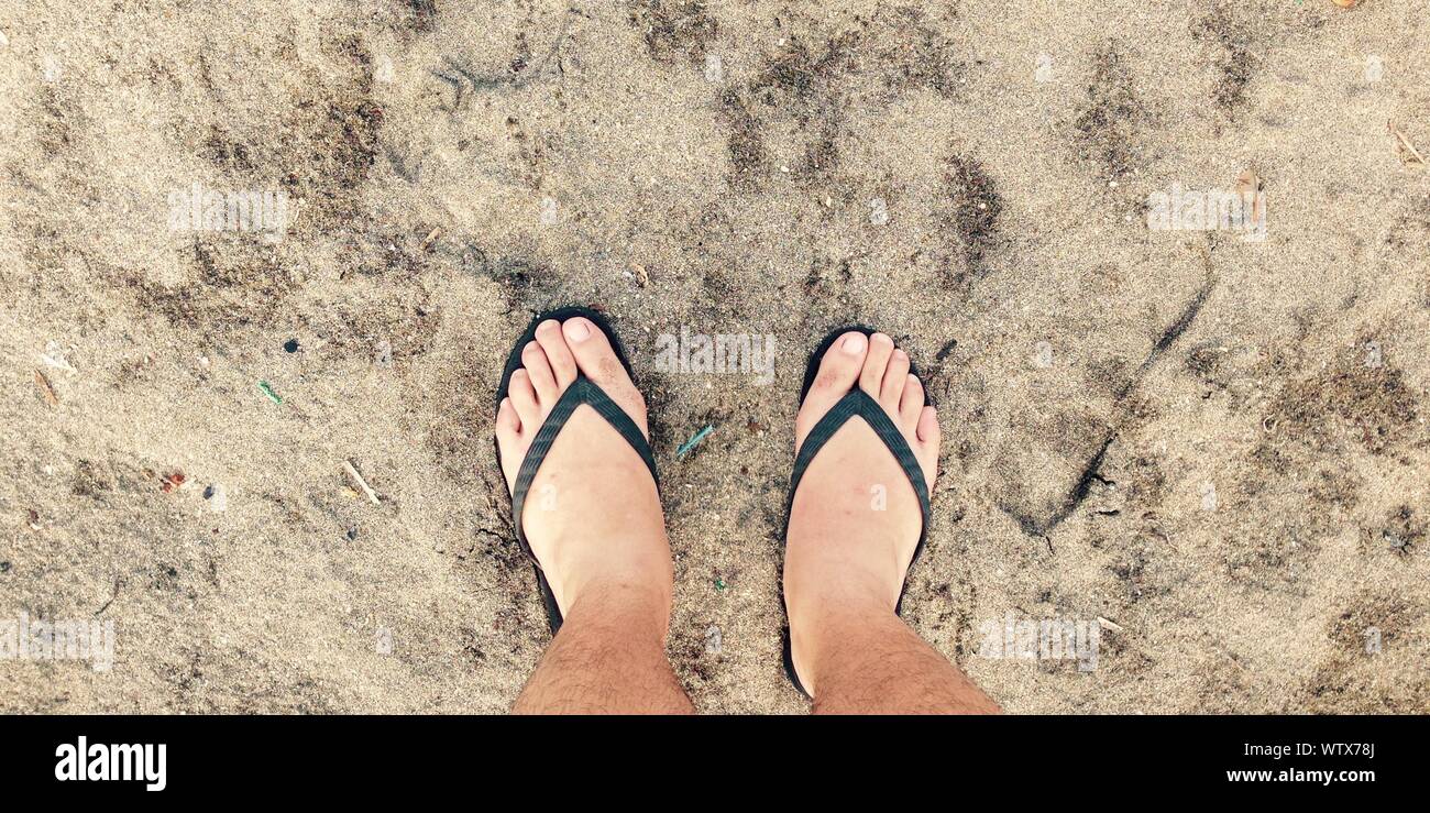 Bajo la sección de hombre vestido con chanclas de pie sobre arena  Fotografía de stock - Alamy