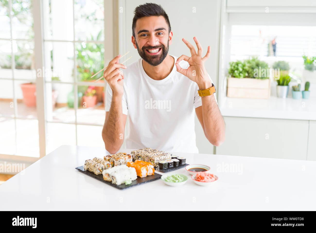 Apuesto Hombre Hispano De Comer Sushi Asiaticos Usando Palillos Chinos Haciendo Bien Firmar Con Los Dedos Simbolo Excelente Fotografia De Stock Alamy