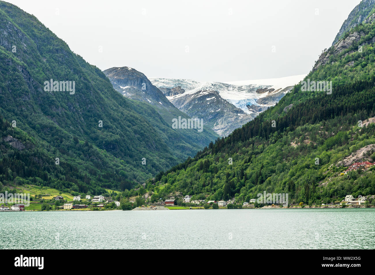 El glaciar Folgefonna cap en las montañas con el lago y el pueblo en primer plano, Odda, región de Hardanger, condado de Hordaland, Noruega Foto de stock