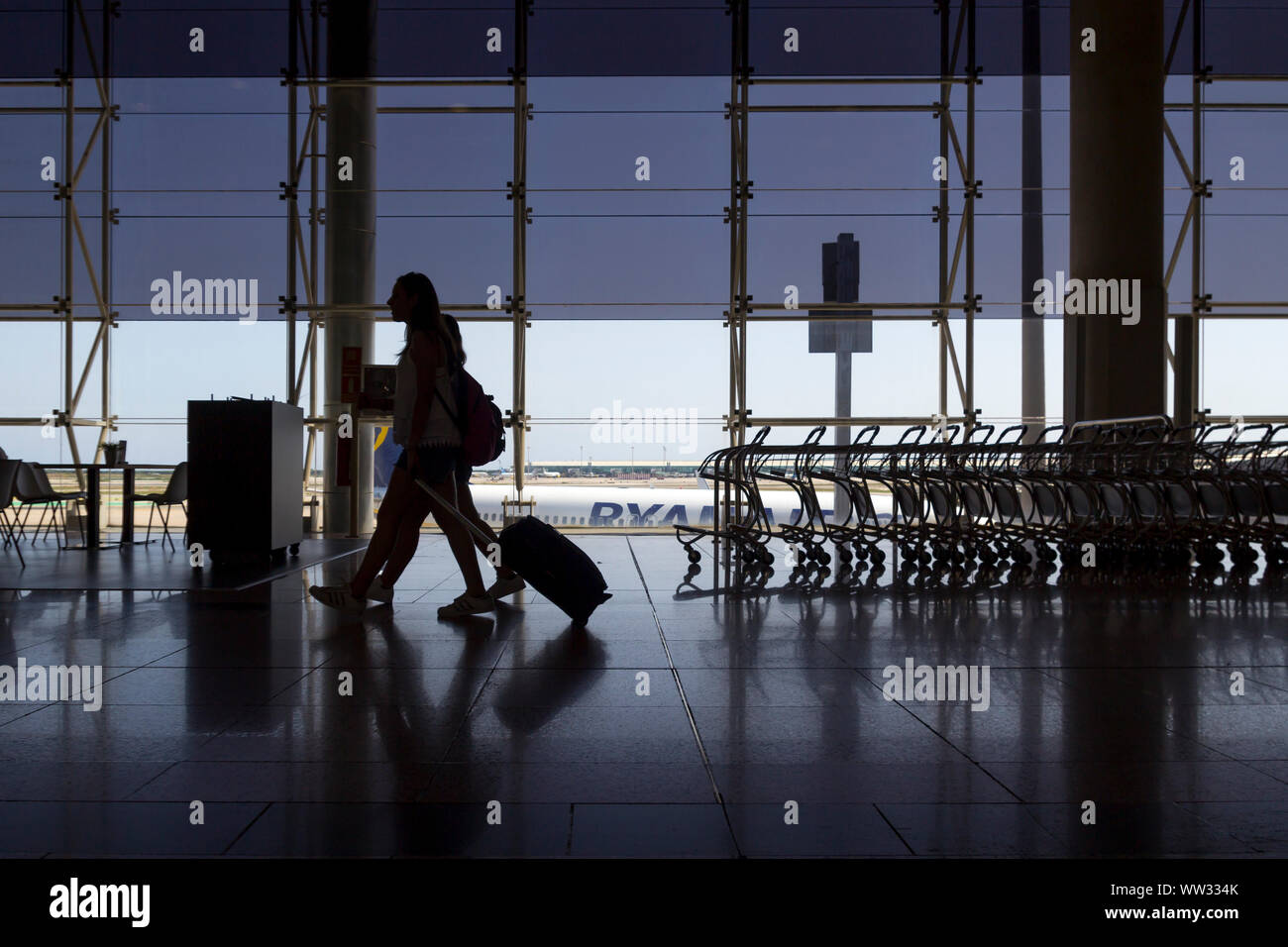 Caminar con equipaje de pasajeros en la terminal del aeropuerto, con aviones de Ryanair en el fondo Foto de stock