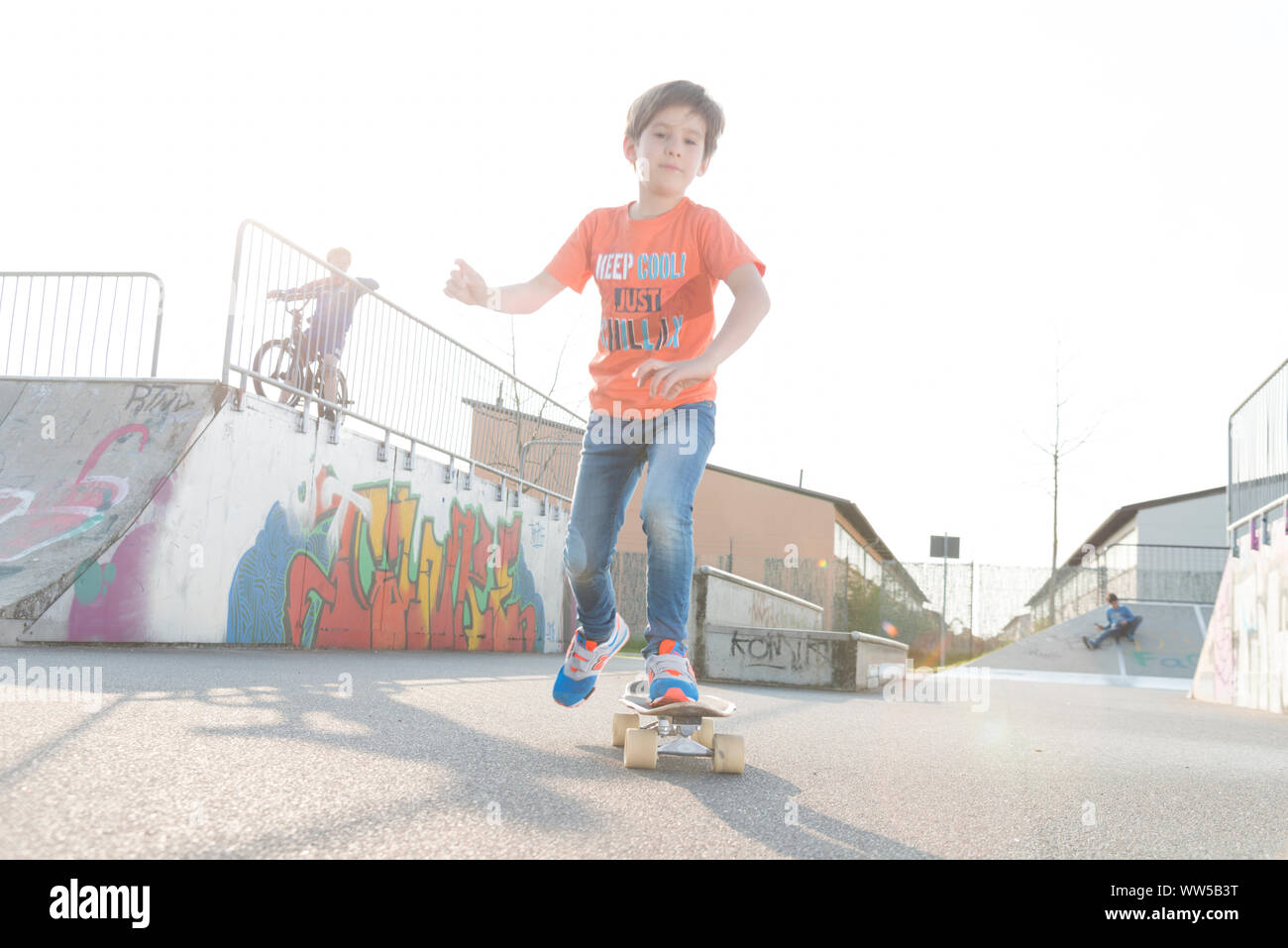 Chico en la camiseta naranja montando skateboard Foto de stock