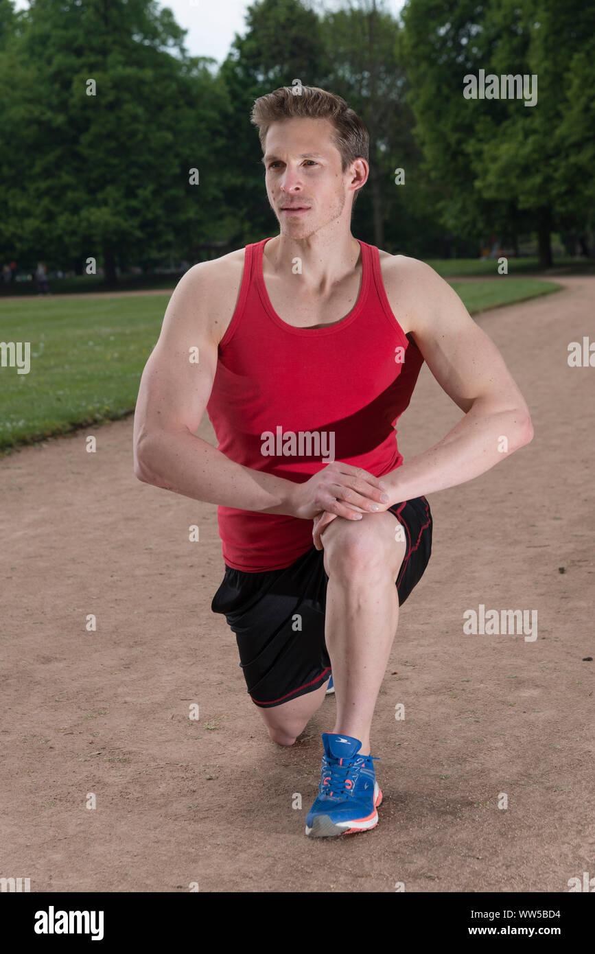 Hombre en ropa deportiva, arrodillado, ejercicio de estiramiento Foto de stock