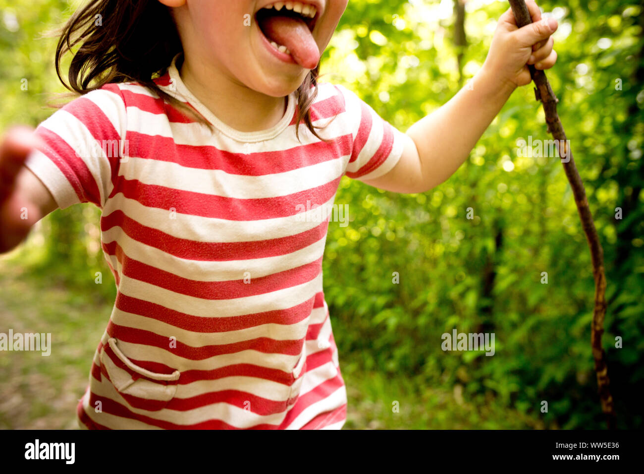 Niño 4-6 años con camisa a rayas y palo en la mano corriendo a través del bosque, de cerca, detalle Foto de stock