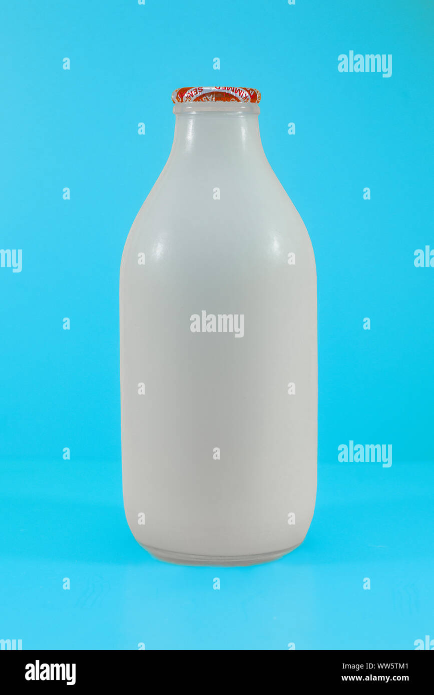 Botella de leche de vidrio reciclable con leche fresca sobre fondo azul. Foto de stock