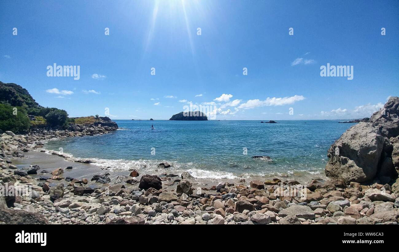 Bay con piedras en la playa y la isla en el horizonte en el mar en Nueva Zelanda Foto de stock
