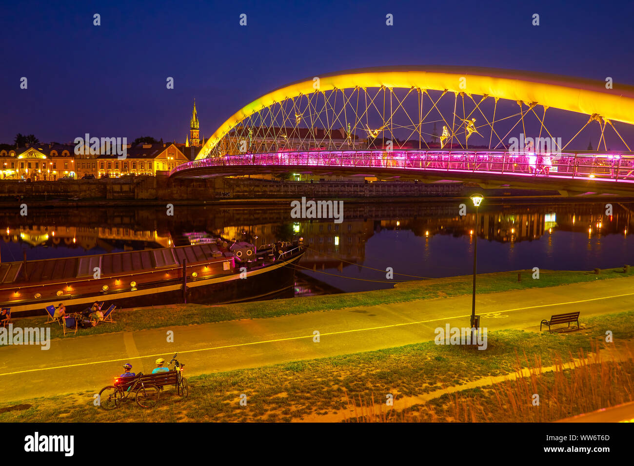 Cracovia, Polonia - Junio 20, 2018: la juventud descansar sobre la hierba, junto a la brillante iluminado Padre Bernatek pasarela a través del río Vístula, el 20 de junio Foto de stock