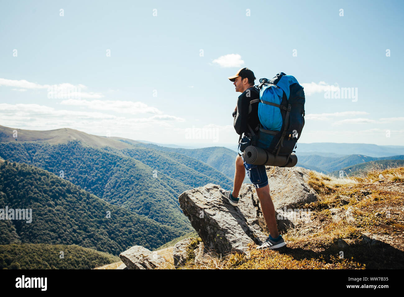 Joven con mochila de pie en la cima de la montaña Foto de stock