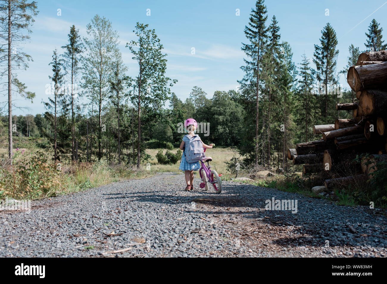Niña caminando a casa de la escuela con su bicicleta en el campo Foto de stock