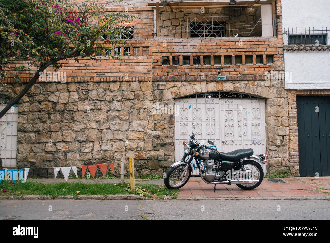 Se asienta en una motocicleta estacionada en la acera de enfrente de la puerta de un garaje en una casa en uno de Bogotá más opulentos suburbios del norte, Colombia Foto de stock