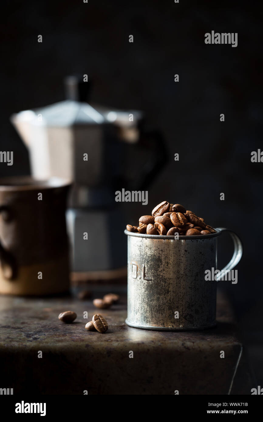 Los granos de café en una taza medidora de estaño contra el oscuro fondo rústico. Low Key con poca profundidad de campo. Foto de stock