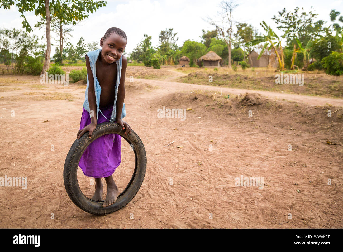 Retrato de una niña de aldea en una falda púrpura jugando con un neumático, distrito de Tororo (Uganda) Foto de stock