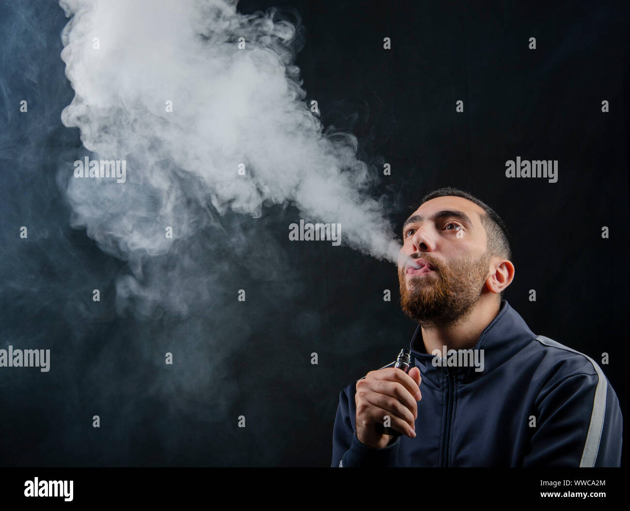 hombre sosteniendo un cigarrillo electrónico de vape o un cigarrillo  electrónico con humo blanco sobre un fondo negro Fotografía de stock - Alamy