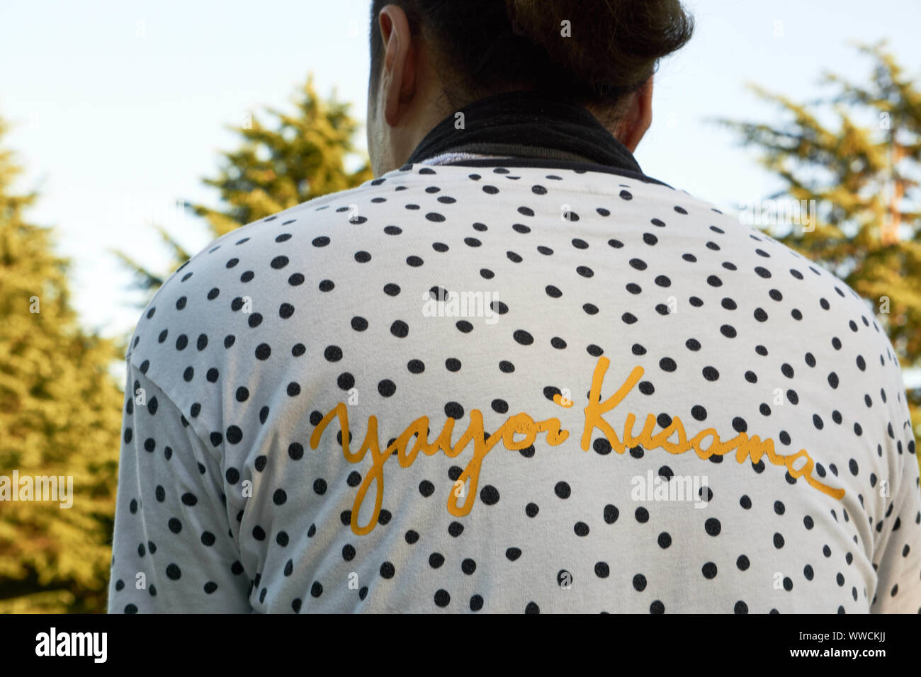 parte posterior de un hombre que una camiseta blanca de Yayoi Kusama con lunares negros y letras amarillas Fotografía de stock - Alamy