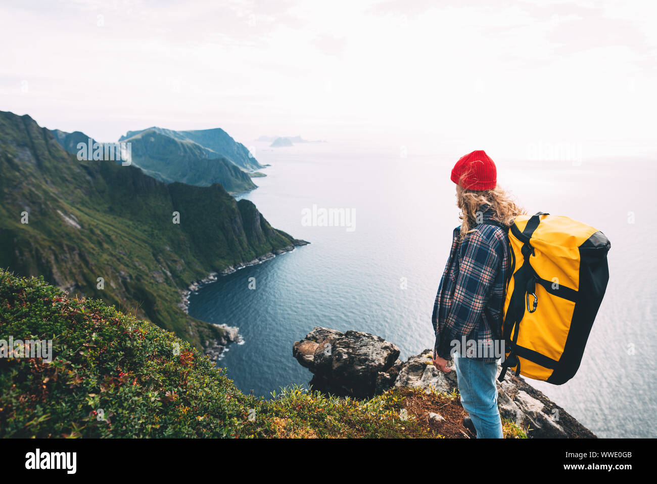 Valiente viaje turístico en altas montañas sobre el mar. Hipster viajero con mochila de pie en el borde Acantilado de roca. Aventura en el estilo de vida wanderlust Foto de stock