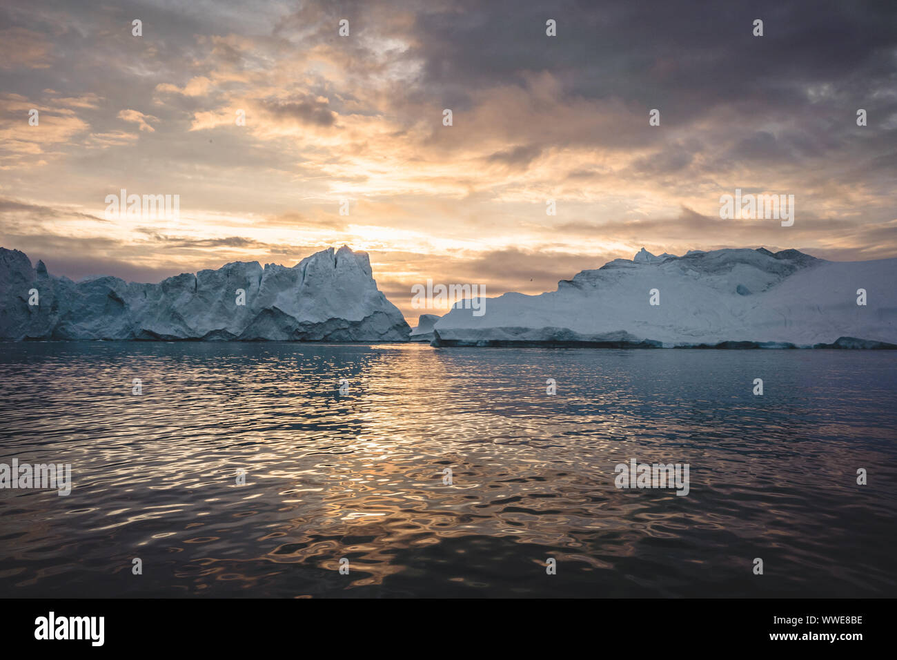 Naturaleza del paisaje ártico con icebergs en Groenlandia icefjord con sol de medianoche atardecer amanecer en el horizonte. Temprano en la mañana de verano durante alpenglow Foto de stock