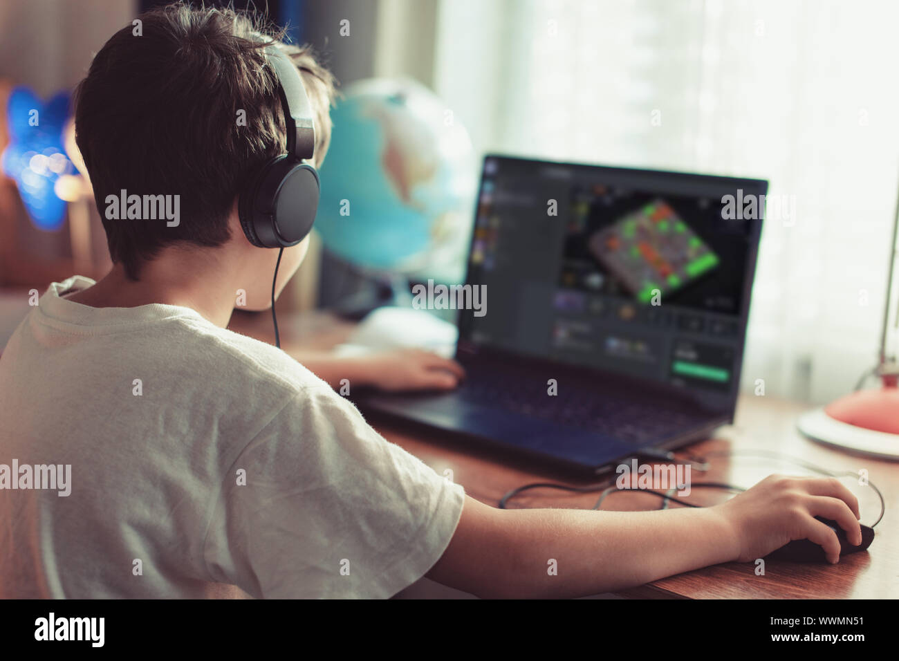 Poco dependiente gamer boy jugando juego multijugador masivo sobre el portátil en casa Foto de stock