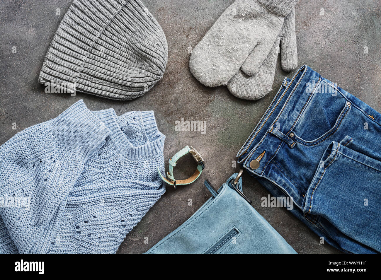 Conjunto de la mujer ropa de invierno y otoño. Blue jeans, suéter de  tejidos, bolsa de cuero azul, relojes, guantes y un sombrero gris oscuro  sobre un fondo de textura Fotografía de