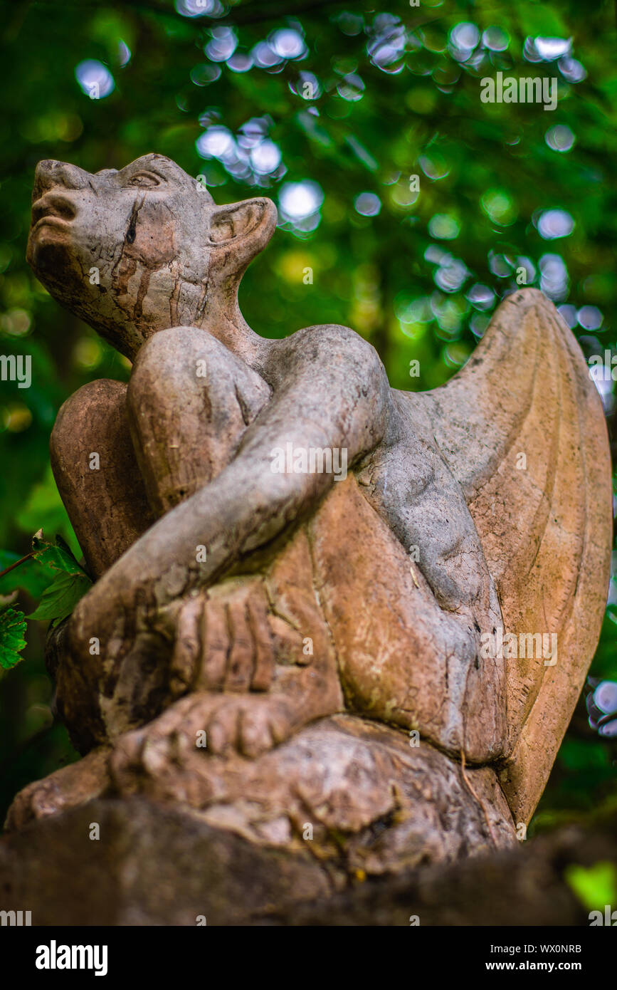 Cerca de la estatua de una gárgola con frondoso jardín Bokeh de fondo Foto de stock