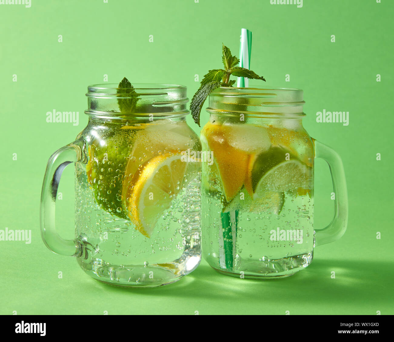Mojito alcohólica natural en frío con burbujas de aire. Dos de vidrio jarra mason con cócteles artesanales sobre un fondo verde. Foto de stock