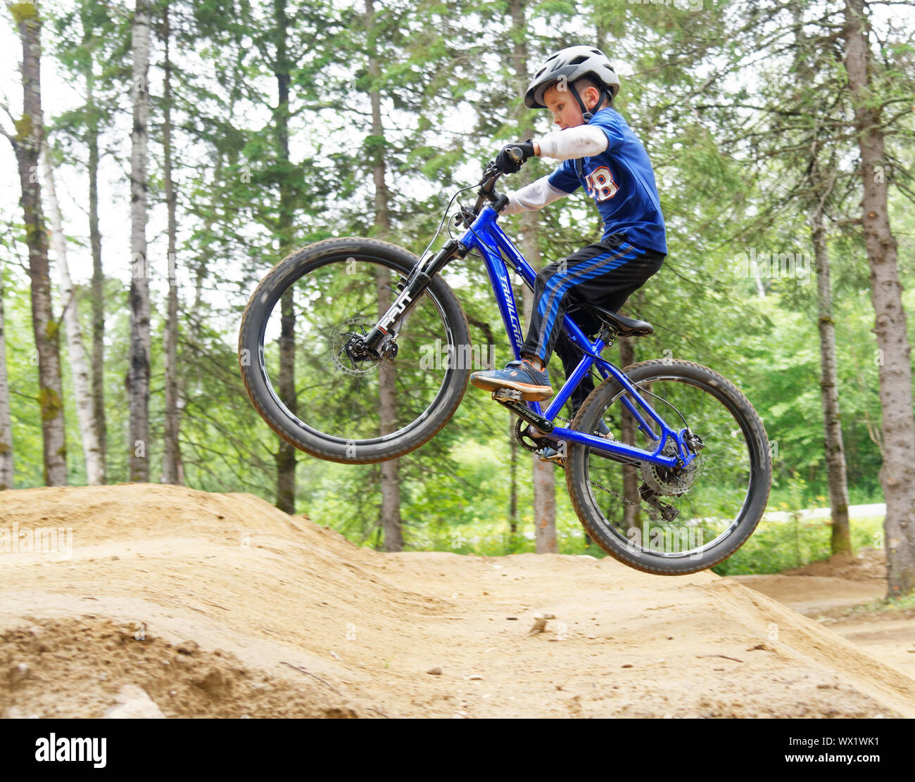 Un niño de siete años haciendo salta sobre su bicicleta de montaña Foto de stock