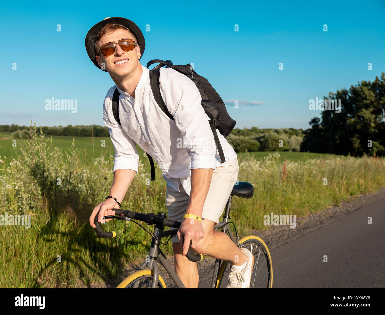 Joven en blanco goza de ciclismo a través de campo Foto de stock