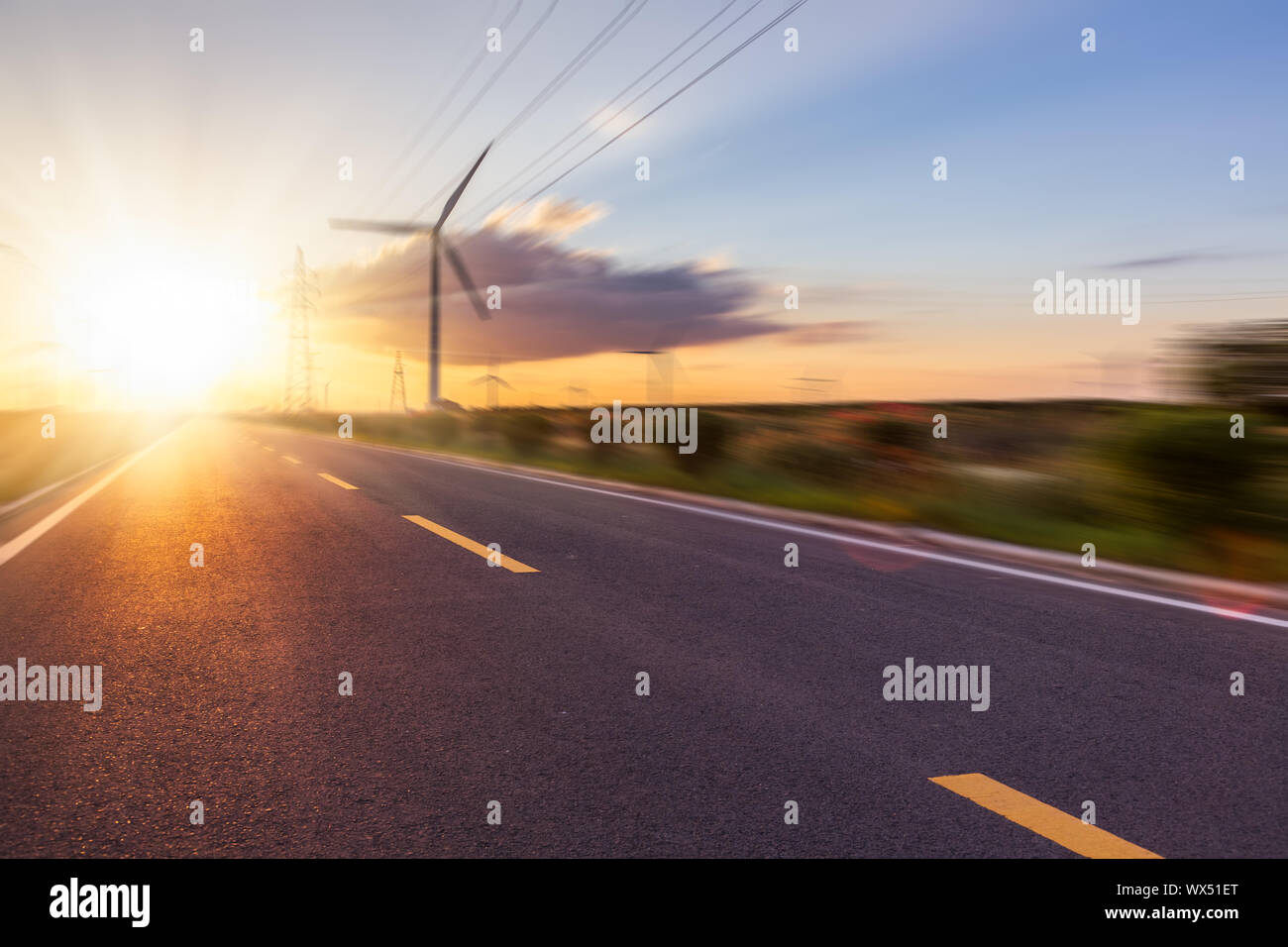 Los aerogeneradores en el paisaje a lo largo de carretera vacía contra el cielo Foto de stock