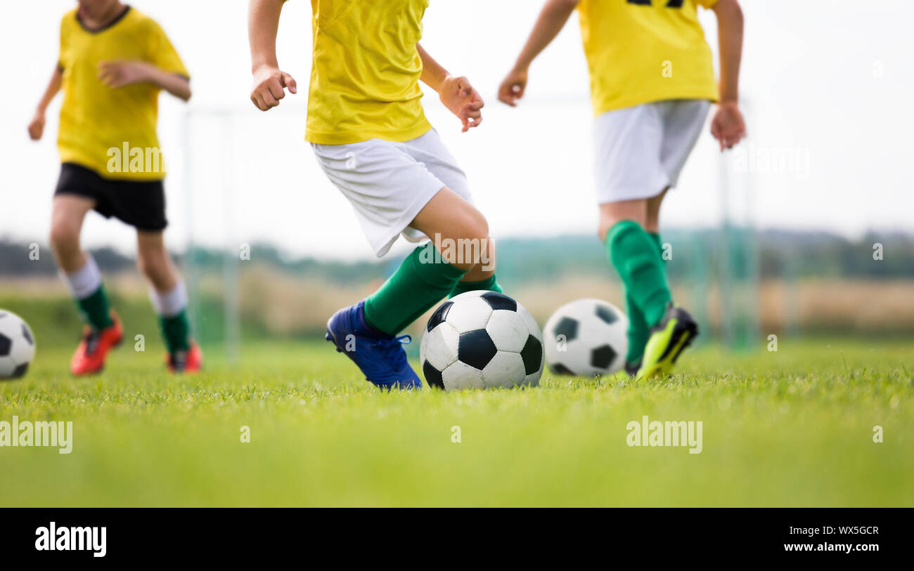 Campamento de fútbol para niños. Niños practican el regate en un campo. Los jugadores de fútbol de desarrollar buenas habilidades para el regate. Los niños en camisas amarillas formación con bolas. Foto de stock