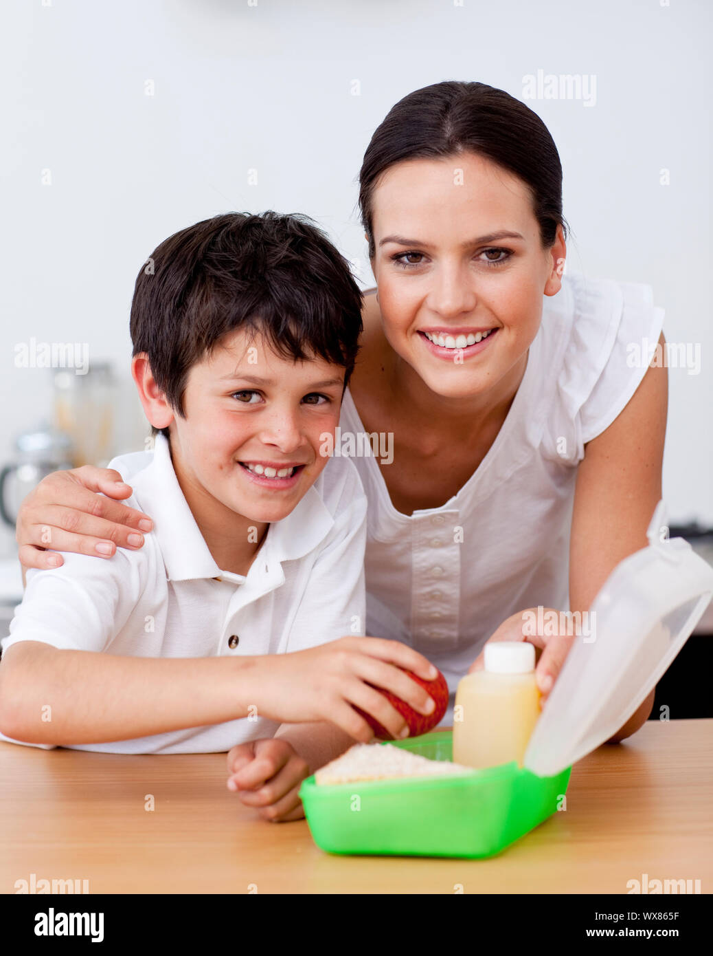 La madre y el hijo sonrientes haciendo el almuerzo escolar en la cocina Foto de stock