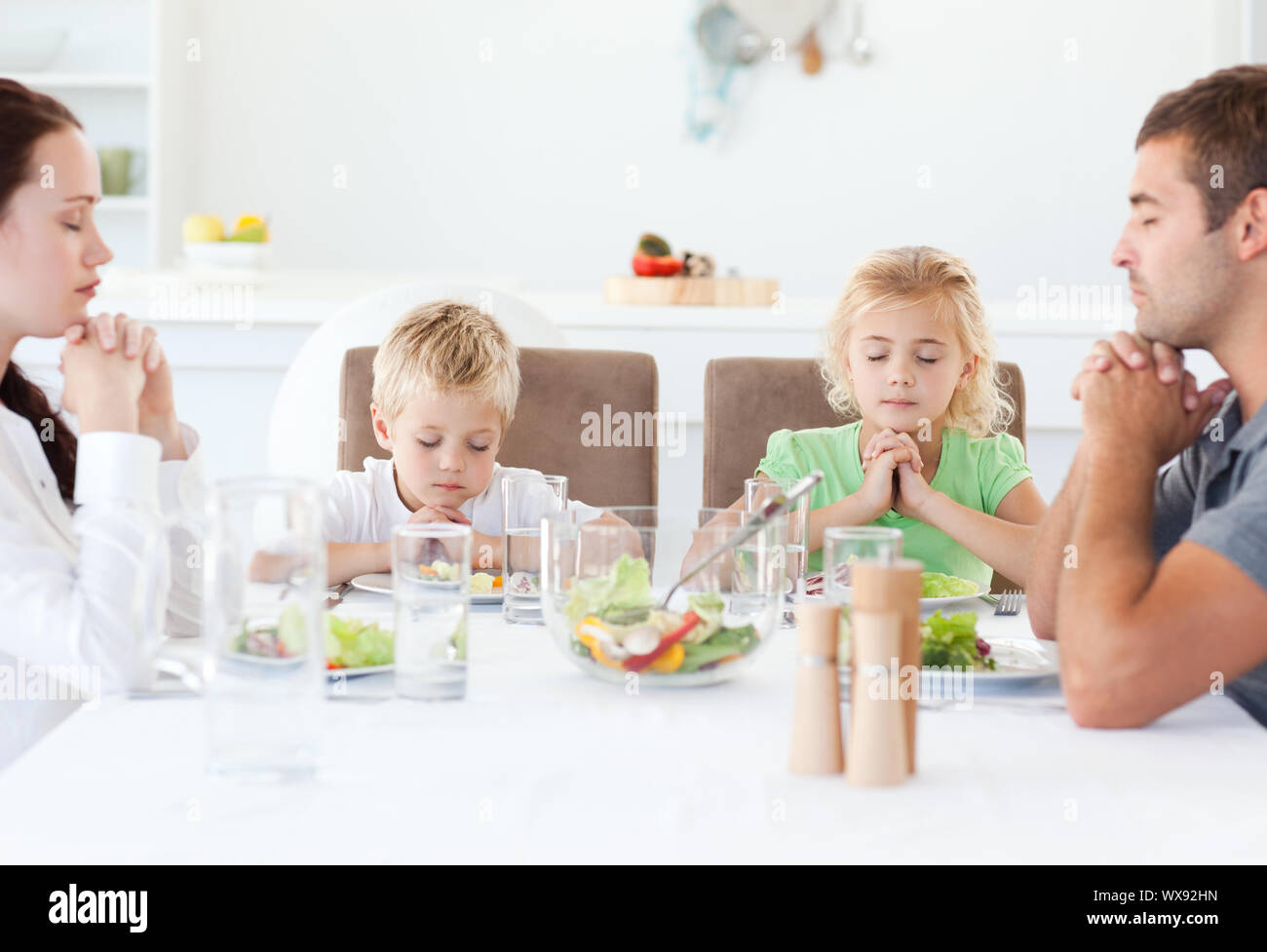 Retrato de una familia orando juntos durante el almuerzo en la cocina