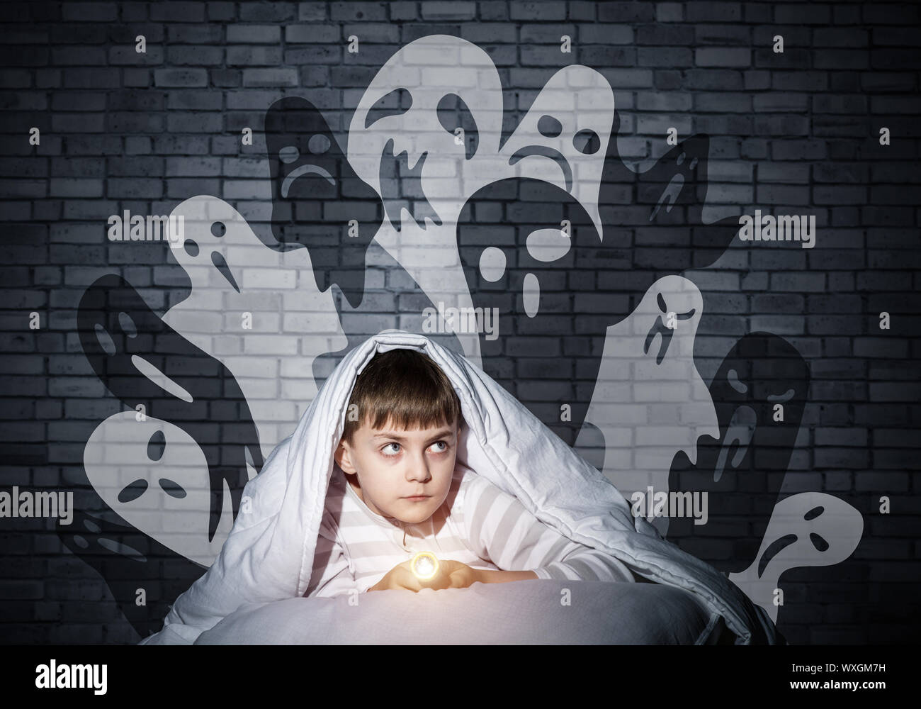 Niño asustado con linterna escondido debajo de una manta. Scary Halloween Monstruos Fantasmales en la pared. Asustado cabrito en pijamas en su cama, en su casa. Miedo Foto de stock