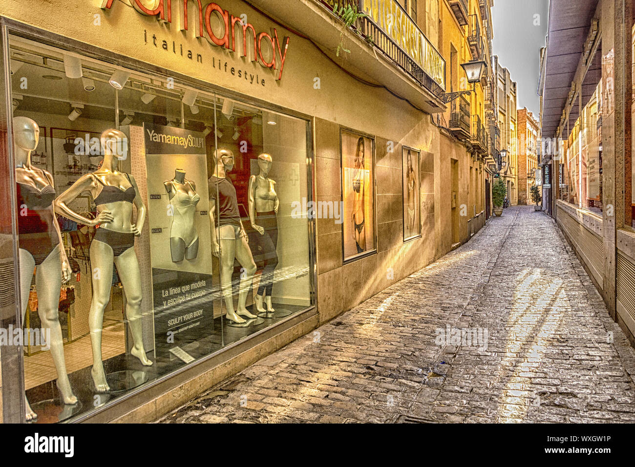 Una calle de piedra en Sevilla, España, flanqueada por los frentes de tiendas con boutiques de ropa de alta gama. Foto de stock