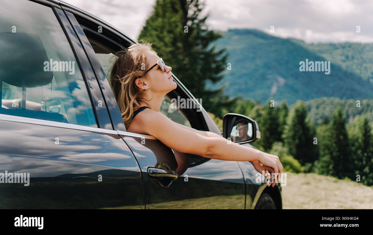 Feliz mujer viaja en coche por las montañas. Concepto de vacaciones de verano. Mujer afuera de la ventana disfrutando de Mountain View Foto de stock