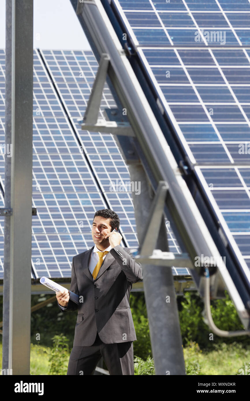 Retrato de mediados adulta italiana ingeniero macho celebración anteproyectos en estación de energía solar y hablando por teléfono móvil. De forma vertical, vista lateral. Copiar spa Foto de stock