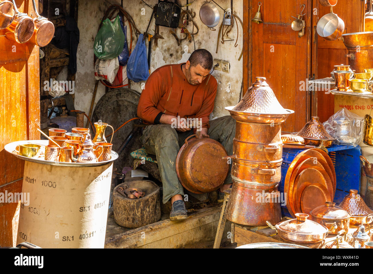 Hombre en un taller/fábrica de artículos de cobre hechas a mano, vasijas, jarras sartenes en muchos estilos diferentes, Fez, Marruecos Foto de stock